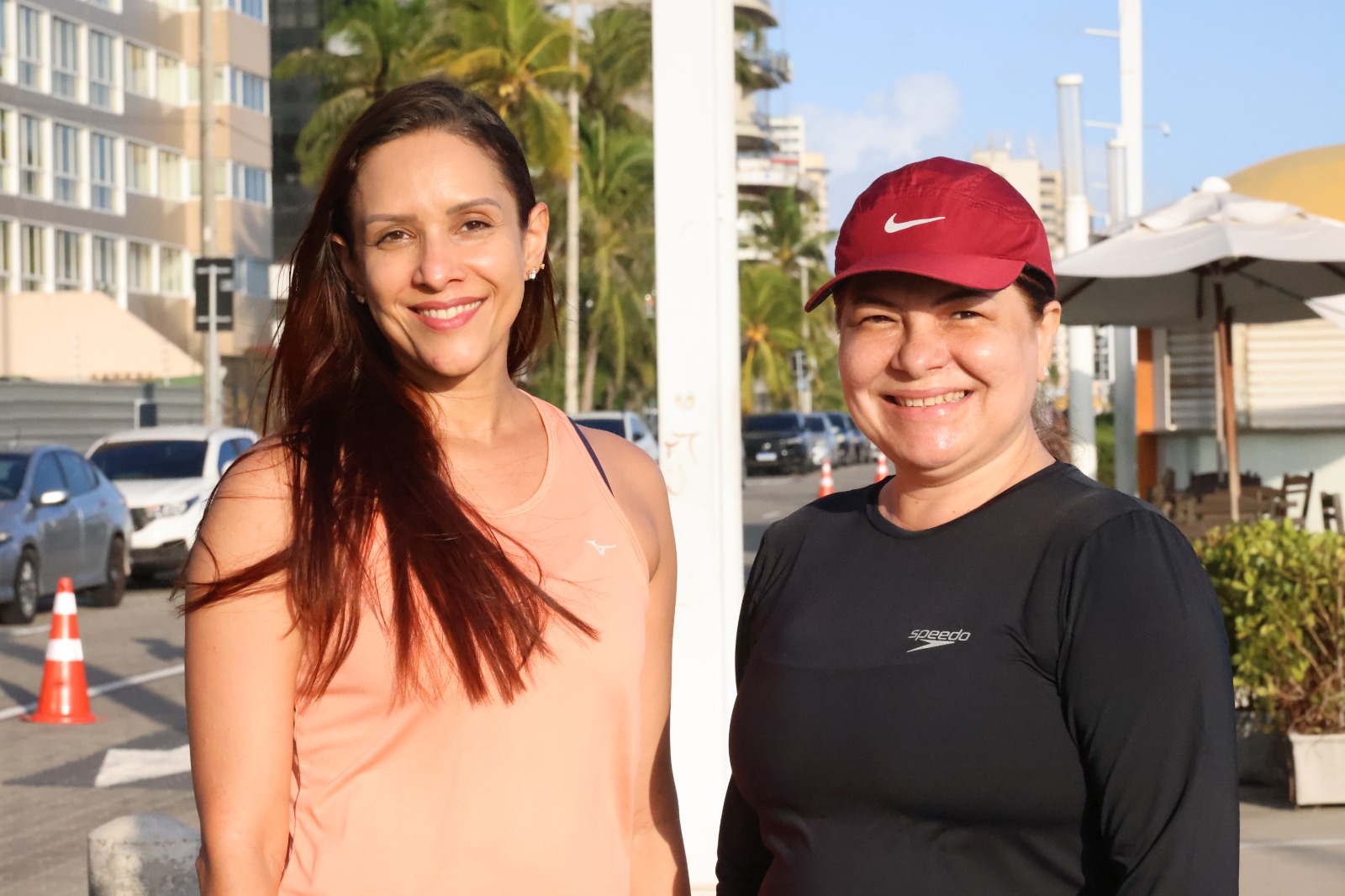 Isabel Soares, de camiseta rosa e cabelo solto, e e Elis Alcântara, de camiseta preta e boné. As duas são mulheres brancas cis-gênero